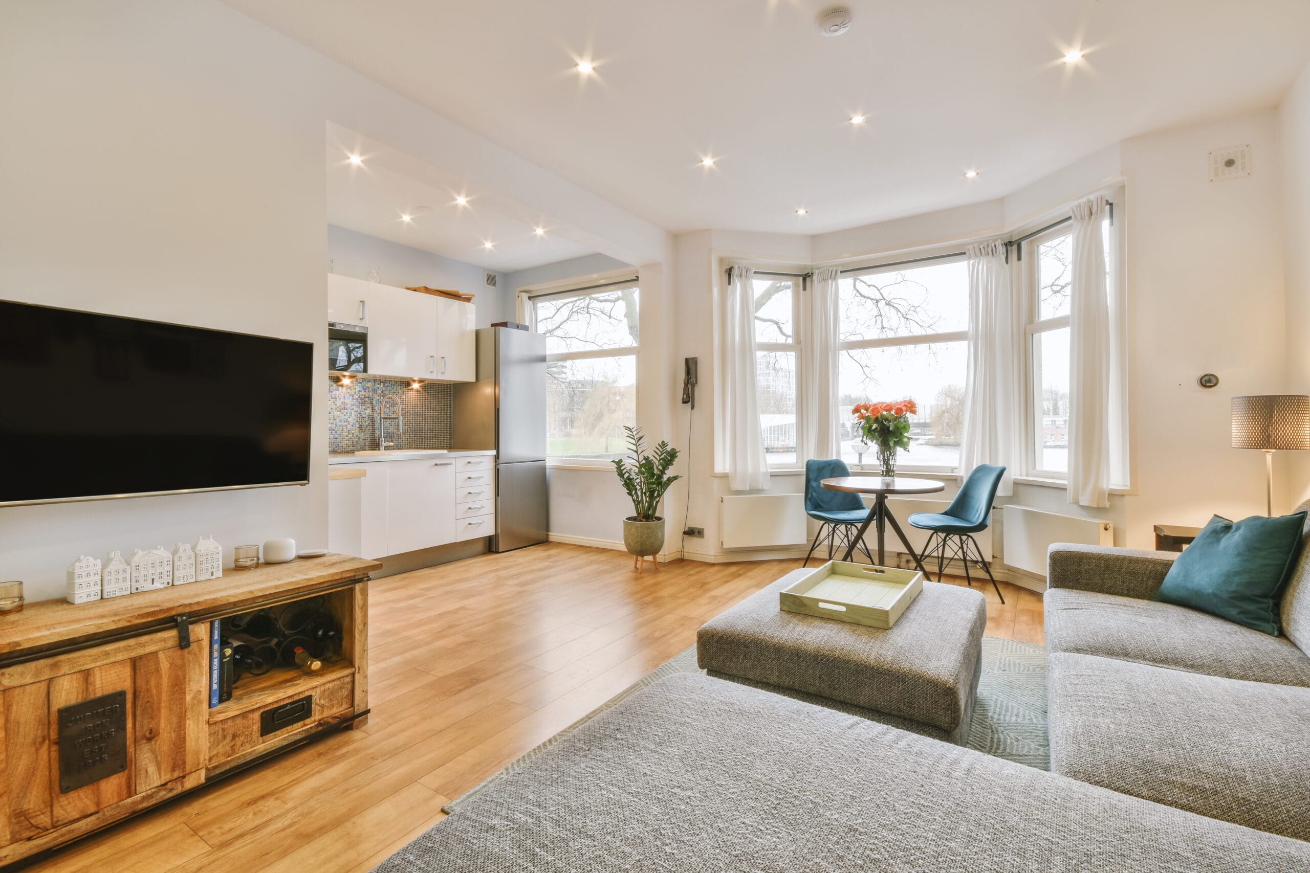 Comfortable armchairs and couch placed near lamps and shelf with TV and dining zone with kitchen against window in modern living room